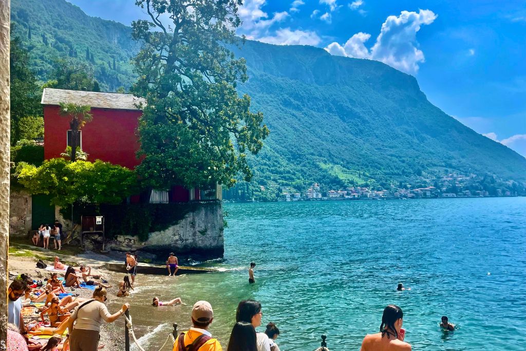A serene beach in Varenna with calm waters and a backdrop of lush green hills