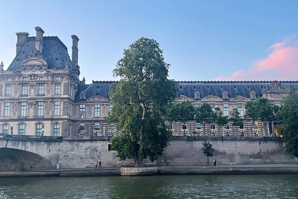 The Louvre Museum viewed from the Seine River, with historic façades and classic Paris riverfront scenery.